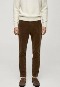 Rjave kordurojske hlače s slim fit krojem, ki imajo mehak izgled in dva stranska žepa, v kombinaciji z rjavimi loafers čevlji in belim puloverjem.