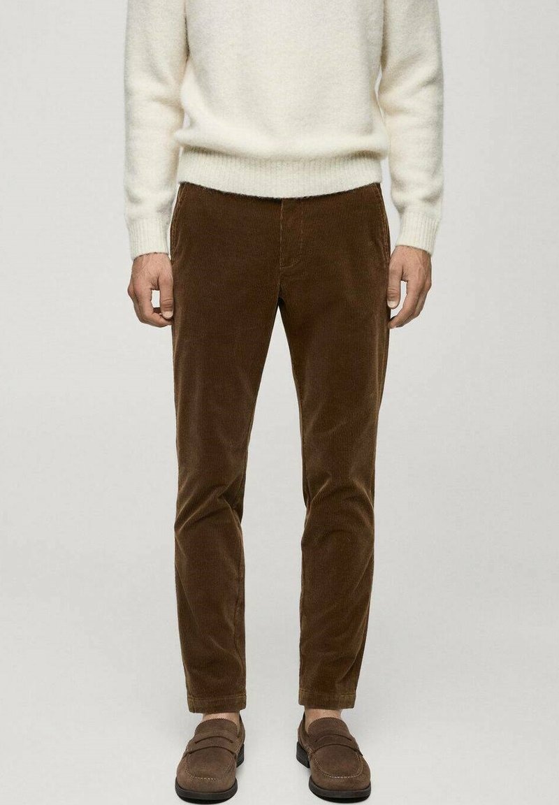 Rjave kordurojske hlače s slim fit krojem, ki imajo mehak izgled in dva stranska žepa, v kombinaciji z rjavimi loafers čevlji in belim puloverjem.