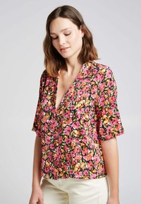 Blouse florale à manches courtes, avec un fond noir et des fleurs vibrantes roses, oranges et jaunes. Design en V avec détail de bouton.