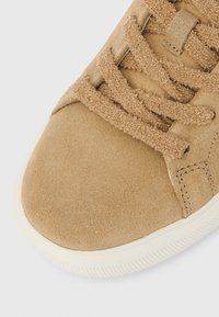 Ταμπά σουέντ αθλητικό παπούτσι με υφή, επίπεδα κορδόνια και λαστιχένια σόλα. Στρογγυλερή μύτη και αντίθετη λεπτομέρεια ραφής.