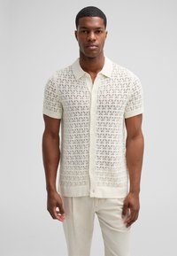 Kurzärmeliges gehäkeltes Strickhemd in Off-White mit Knopfverschluss auf der Vorderseite, ausgestattet mit einer strukturierten offenen Webart sowie einem gerippten Kragen und Saum.