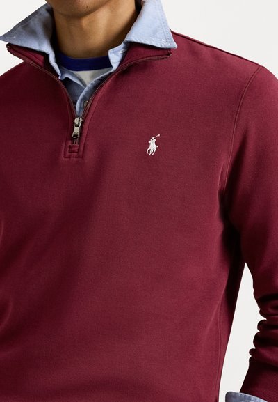 Pulover bordeaux cu un design cu jumătate de fermoar și o cămașă albastră cu guler dedesubt; cu un mic logo alb pe piept. Material din bumbac.