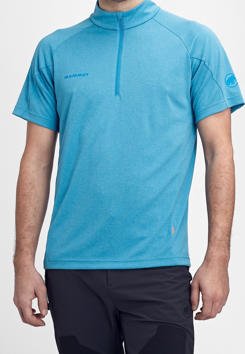 Ljusblå kortärmad skjorta med hög krage, med en främre halvdragkedja och subtil textur. Varumärkeslogotyp på bröstet och ärmen.