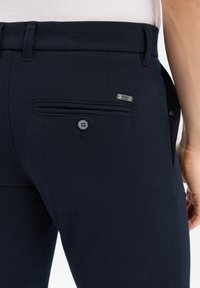 Granatowe spodnie teksturowane z tylną kieszenią, posiadające zapięcie na guzik i małą metalową metkę z logo na pasku.