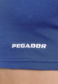 Blå ribbet stoff, med hvit brodert tekst "PEGADOR" nederst. Designet er enkelt og tettsittende med en glatt tekstur.