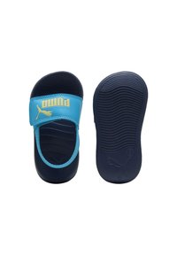 Een paar navyblauwe en lichtblauwe Puma schuifsandalen, waarbij de ene bovenkant met band wordt getoond en de andere de gestructureerde zool laat zien.