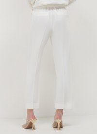 Pantalon blanc à coupe décontractée, taille élastique et ourlets retroussés, associé à des mules à talons dorés avec un détail en maille complexe.