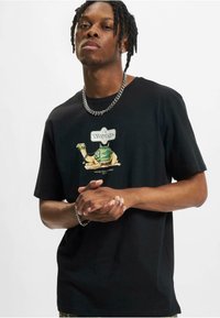Sort bomulds t-shirt med et grafisk motiv af en kamel med grønne accenter og teksten "Voyage". Korte ærmer og afslappet pasform. Sølv kædehalssmykke.