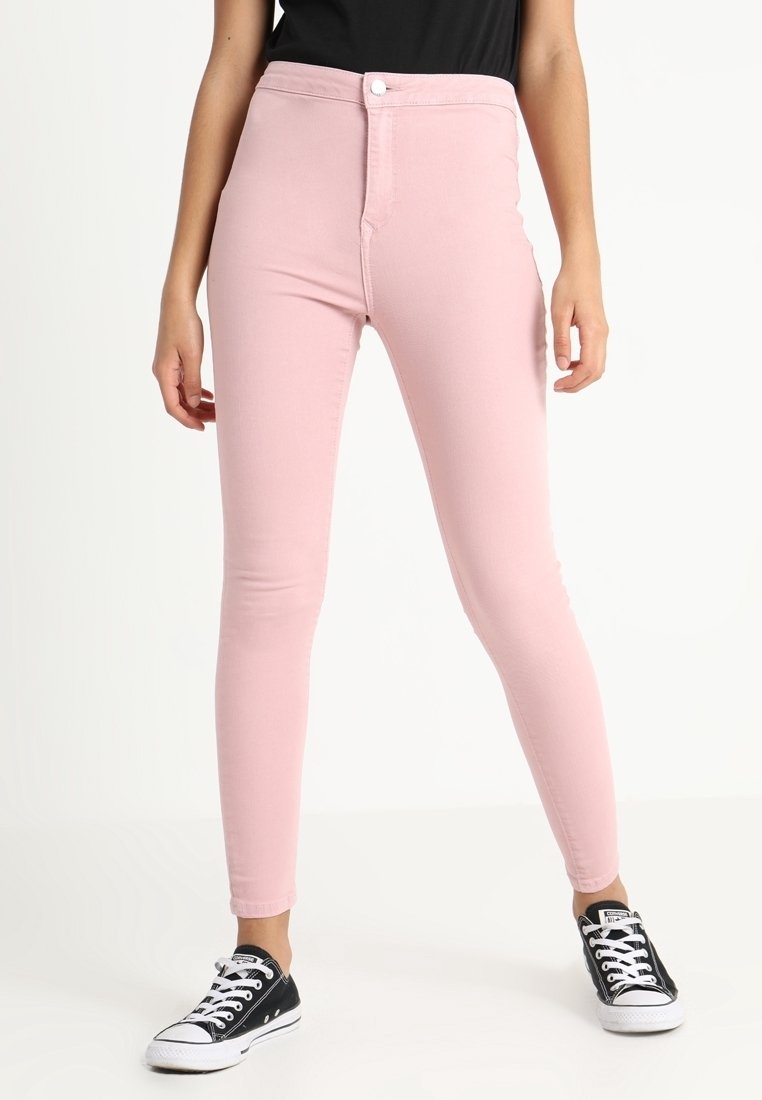 Jeans skinny de mezclilla rosa con cintura alta, cremallera frontal y cierre de botón, combinados con zapatillas negras con suelas y cordones blancos.