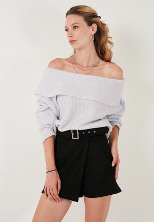 Hellblauer, schulterfreier Pullover mit geripptem Muster, kombiniert mit hochgeschnittenen schwarzen Shorts mit einem Gürtel mit Schnalle.