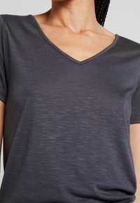 Mörkgrå V-ringad t-shirt i lätt, strukturerad tyg med korta ärmar och avslappnad passform. Diskret horisontell linjemönster.