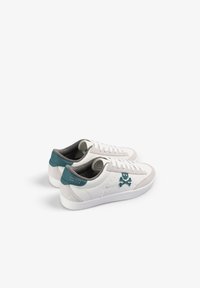 Zapatillas blancas con acentos en teal, detalle de ante y un logo de calavera. Presentan un diseño con cordones y una suela de goma texturizada.