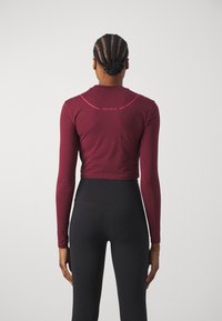 Top corto a maniche lunghe color bordeaux con scollo rotondo, caratterizzato da un accento curvo rosa e la scritta "ONLY PLAY" sul retro, realizzato in un tessuto morbido.