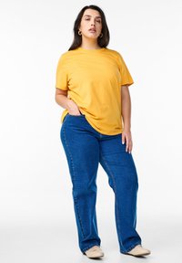 T-shirt jaune à manches courtes associé à un jean en denim bleu. Le t-shirt présente une coupe décontractée et le jean a une coupe droite classique.