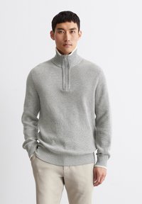 Gray ribbed sweater with a half-zip collar, featuring a textured knit pattern and contrasting inner collar. Paired with light beige pants.