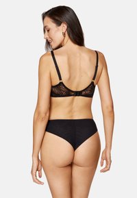 Czarny koronkowy biustonosz braletka z przezroczystym tyłem i regulowanymi ramiączkami, zestawiony z czarnymi bezszwowi bielizną bikini, która ma gładkie, nieprzezroczyste wykończenie.