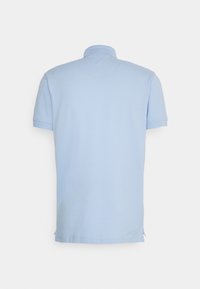 Vaaleansininen lyhythihainen polo-paita, jossa on ribbireunus ja sivuhalkiot helman rentoa istuvuutta varten. Kankaan pinta on sileä kauttaaltaan.