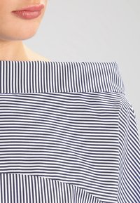 Top a spalle scoperte a righe blu navy e bianche con colletto ampio, caratterizzato da motivi a righe orizzontali e verticali e una vestibilità rilassata.