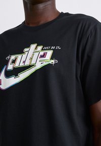 Camiseta de algodón negra con un logo de Nike multicolor en una tipografía estilizada y la frase "SIMPLEMENTE HAZLO". Manga corta, cuello redondo.