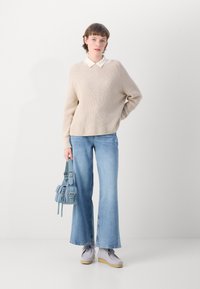 Beige strikket genser, lys blå vid buks, grå sko og en liten blå veske med spenner. Glatt tekstur, uformelt design.