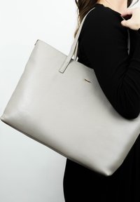 Grijze leren tote bag met een gladde textuur, eenvoudig ontwerp en korte handvatten. Beschikt over een kleine gouden accenten aan de voorkant.