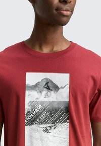 Rode katoenen t-shirt met een grote zwart-wit graphic van bergen, een snowboarder en tekstelementen. Klassieke ronde halslijn.