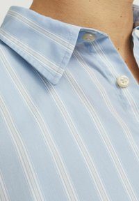 Camisa de rayas azul claro con cuello puntiagudo, que presenta finas rayas blancas y beige y un solo botón en el cuello. Textura de tejido suave.