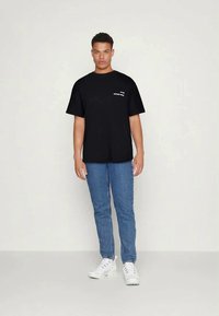 Camiseta de algodão preta com um corte largo, mangas curtas e texto branco no peito. Combinada com jeans de ganga azul claro e ténis brancos.