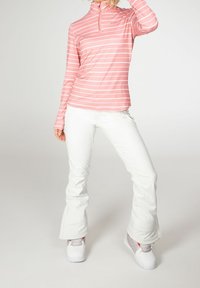 Růžový a bílý pruhovaný top s dlouhým rukávem a polozipem, kombinovaný s bílými kalhotami a bílou obuví, předvádějící přiléhavý střih.