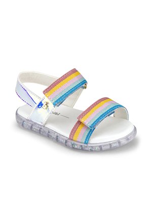 Dziecięca sandałka z przezroczystą podeszwą i tekstylnymi paskami z poziomymi paseczkami w tęczowych kolorach: różowym, żółtym, niebieskim i białym.