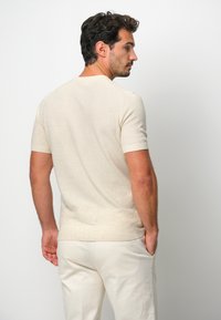 Beiger Kurzarmpullover mit strukturiertem Strickmuster, Rundhalsausschnitt und taillierter Form, kombiniert mit hellen Hosen.