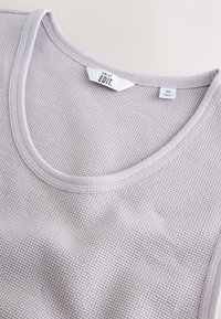 Lichtgrijze tanktop gemaakt van gestructureerde, wafelknoopstof. Heeft een ronde halslijn en een label met maat medium en merk "NEXT EDIT."