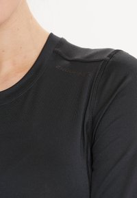 Schwarzes Sportshirt aus glattem, feuchtigkeitsableitendem Stoff. Mit rundem Halsausschnitt und dezentem Logodetail auf der Schulter.