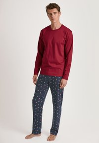 Maglia rossa a maniche lunghe con scollatura rotonda, abbinata a pantaloni del pigiama blu navy con pois bianchi e piccoli motivi floreali rossi.