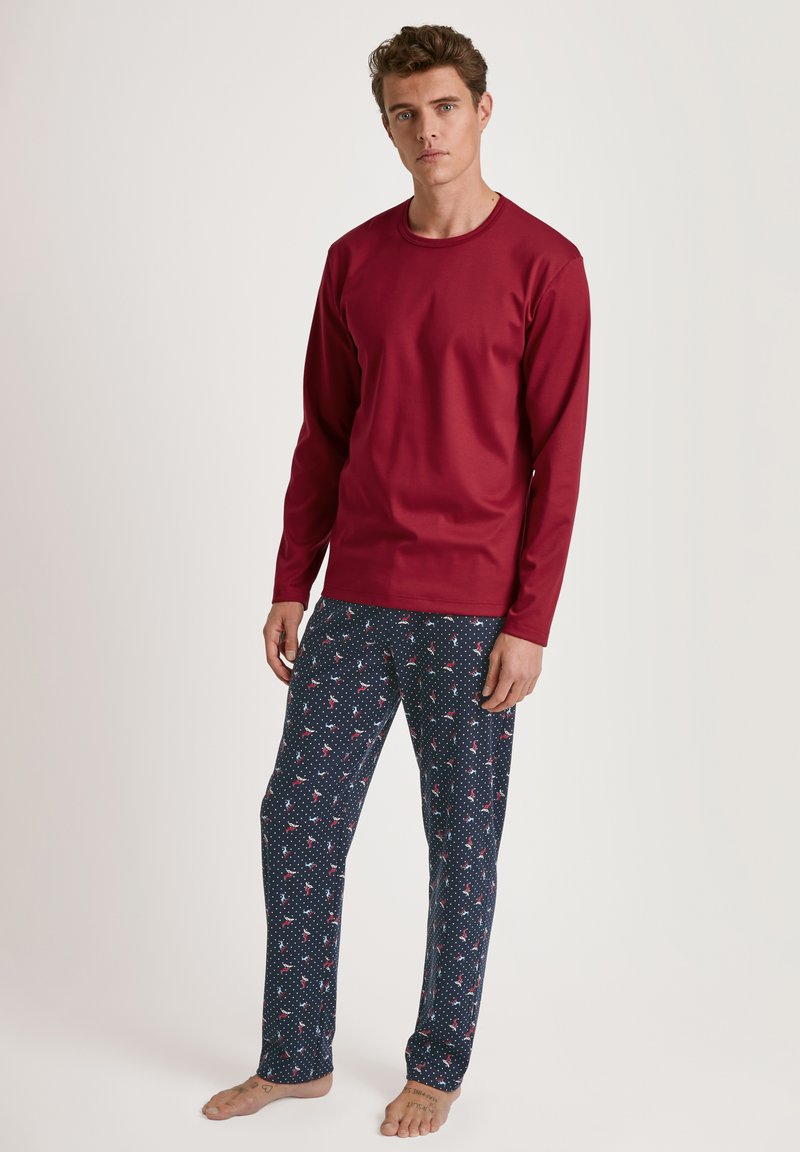 Maglia rossa a maniche lunghe con scollatura rotonda, abbinata a pantaloni del pigiama blu navy con pois bianchi e piccoli motivi floreali rossi.