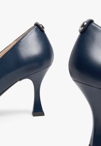 Chaussures à talons en cuir bleu marine au design élégant, à bout pointu et talon courbé. Présentent un accent métallique à l'arrière.