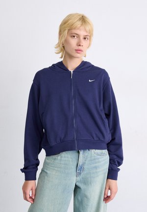 Navy sininen vetoketjuhuppari, joka on valmistettu pehmeästä kankaasta. Hupparissa on etuvetoketju, sivutaskut ja pieni valkoinen logo vasemmassa rinnassa.