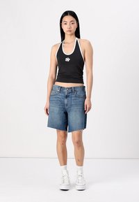 Musta halterneck crop-top valkoisilla yksityiskohdilla ja kukkakuviolla, yhdistettynä vaaleansinisiin farkkushortseihin, joissa on rikottu helma ja taskut. Valkoiset tennarit viimeistelevät asukokonaisuuden.