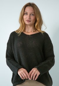 Czarny sweter dzianinowy o luźnym kroju, z teksturowanym splotem i szerokimi rękawami. Dekolt jest nieco głęboki, co podkreśla jego casualowy styl.