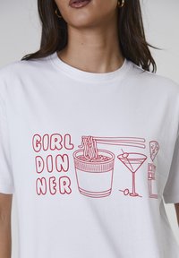 Witte t-shirt met rood grafisch ontwerp met een kom noedels, eetstokjes, een cocktail, een plak kaas en de tekst "GIRL DINNER."