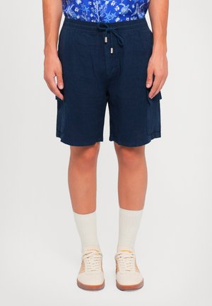 Marineblaue Leinen-Shorts mit einem elastischen Bund und Kordelzug, ausgestattet mit Seitentaschen und einer lockeren Passform, kombiniert mit weißen Socken und Sneakern.