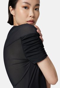 Blusa nera con maniche corte arricciate, realizzata in un tessuto morbido e trasparente. Il design aderente mette in risalto i dettagli delle spalle e del décolleté.