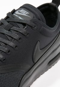 Nærbillede af sort Nike Air Max sneaker, der viser tekstureret stof, snørebånd, Nike swoosh og Air Max-mærket på tungen.