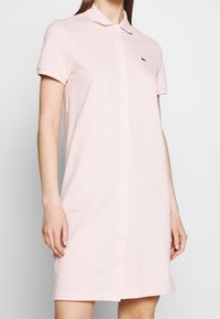 Polo-style dress in soft pink fabric, featuring a button-down front, short sleeves, and an embroidered logo on the chest.