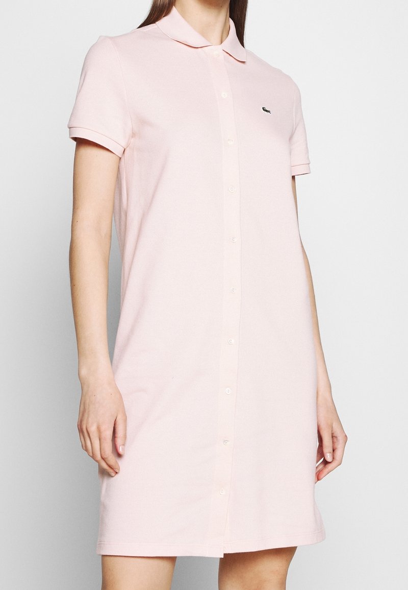 Polo-style dress in soft pink fabric, featuring a button-down front, short sleeves, and an embroidered logo on the chest.