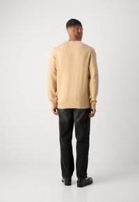 Hellbeige Pullover aus strukturiertem Stoff, mit gerippten Bündchen und Saum. Kombiniert mit schwarzen, geraden Hosen und schwarzen Schuhen.