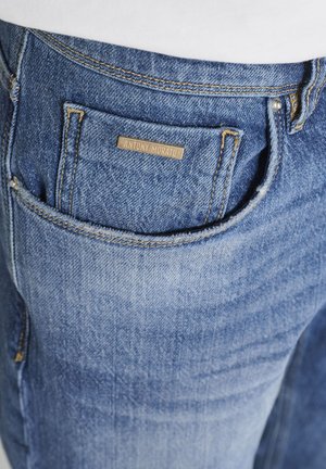 Blauer Denim-Jeans in Nahaufnahme, die die Vordertasche mit einem kleinen Etikett zeigt, auf dem "ANTONY MORATO" in kontrastierender Naht steht.