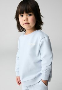 Svetlo modrá mikina z mäkkého materiálu, s teplákovými manžetami a lemom, s logom "ALLSAINTS" v zlatej farbe na prednej strane.