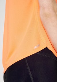 Camiseta deportiva naranja con diseño texturizado, pantalones ajustados en negro contrastante. Detalle de logo cerca del dobladillo.