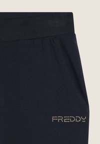 Pantalons de survêtement bleu marine avec une taille côtelée et des poches, portant "FREDDY" en clous argentés sur le côté gauche. Tissu à texture lisse.